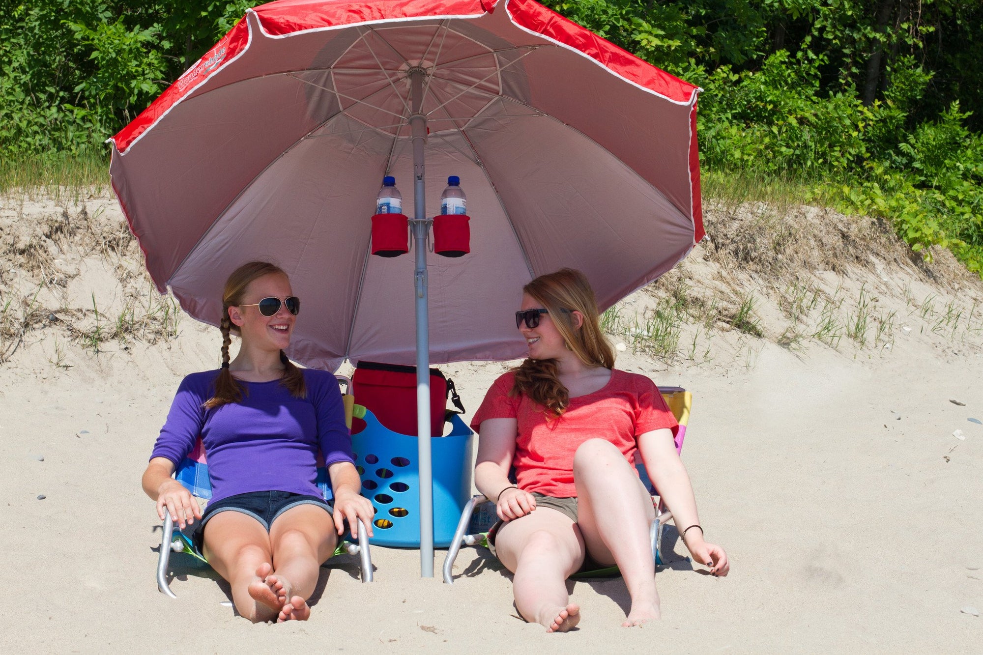 2 women sitting outside at beach under red wondershade